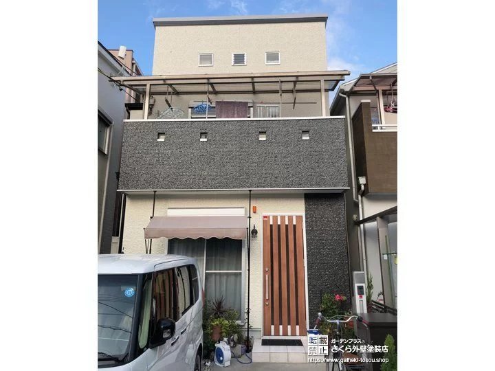 黒に近いダークグレーの外壁と木目の玄関ドア、白い外壁を組み合わせた住宅の正面